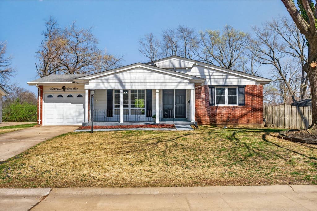 A single-story ranch home with a white garage, columned front porch, and red brick wing under a bright blue sky